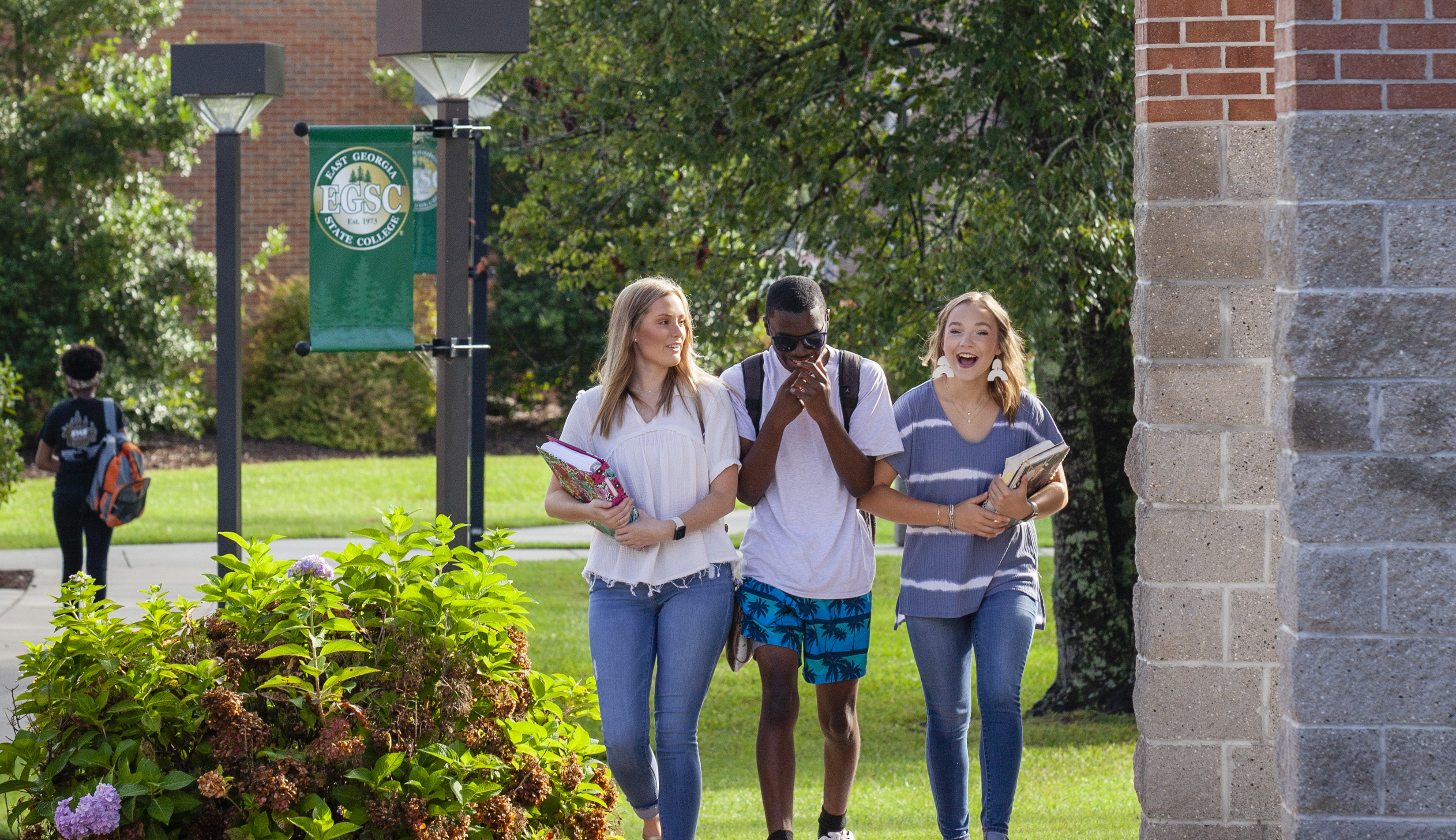 two female students and a male student laughing while walking through campus